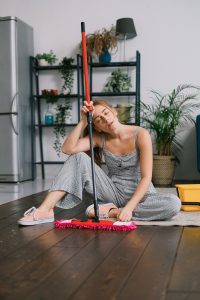 A tired woman rests on the floor with a mop
