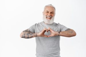 A middle-aged man with tattoos makes a heart shape with his hands. Image by cookie_studio on Freepik.