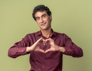 a middle-aged man in a red shirt makes a heart shape with his hands. Image by stockking on Freepik