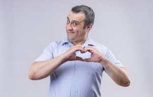 a middle-aged man makes a silly face while also making a heart shape with his hands. Image by stockking on Freepik