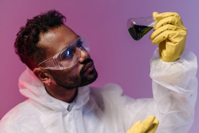 A scientist looks quizzically at a small beaker containing mysterious coloured liquid